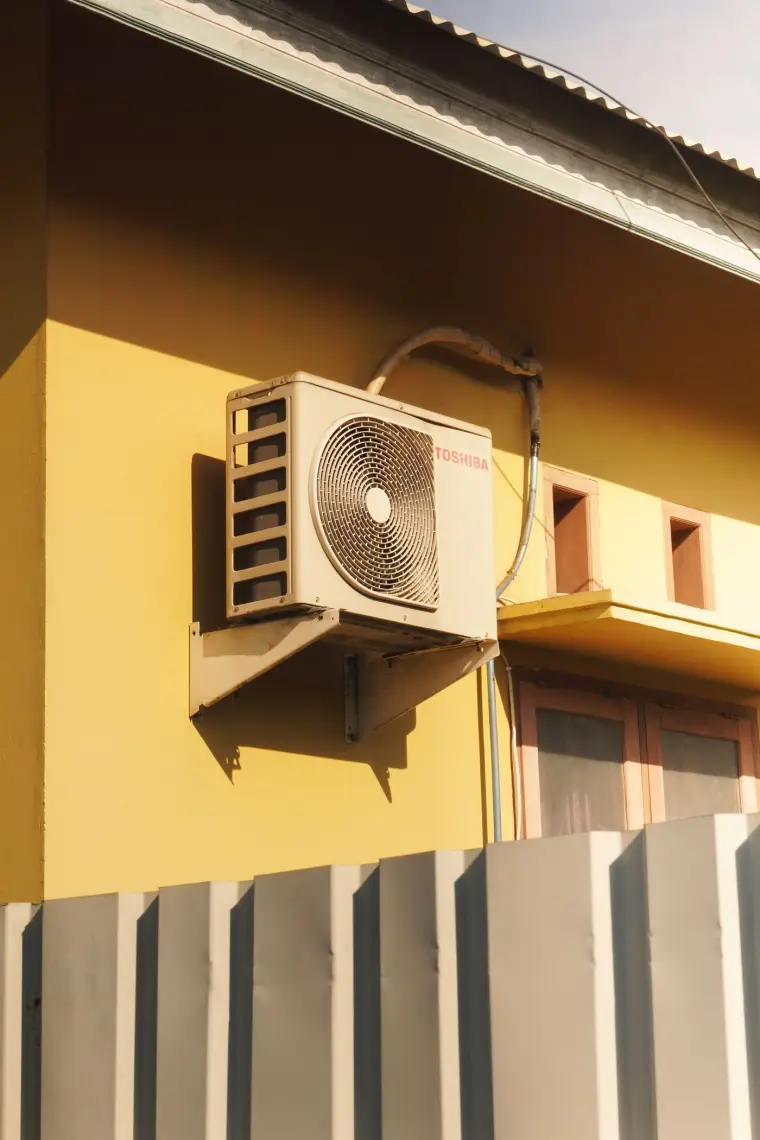 Unidad exterior de aire acondicionado instalada sobre un soporte metálico en la pared de una casa